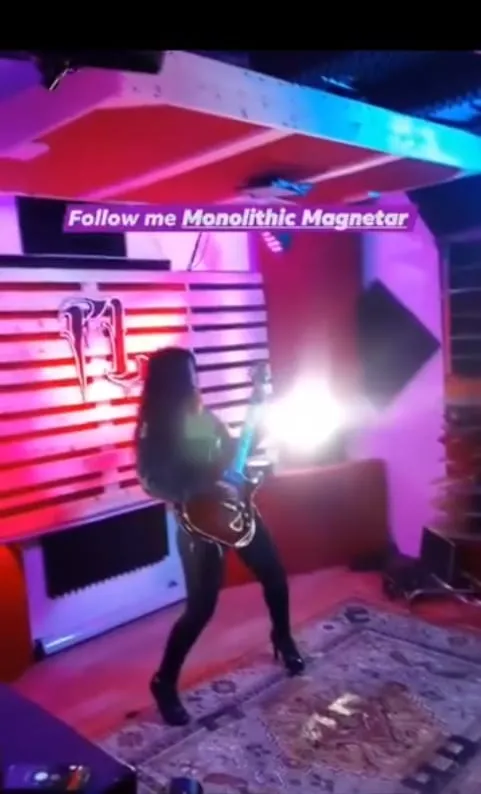 A guitarist silhouetted against a burst of white light in a magenta-lit rehearsal space.